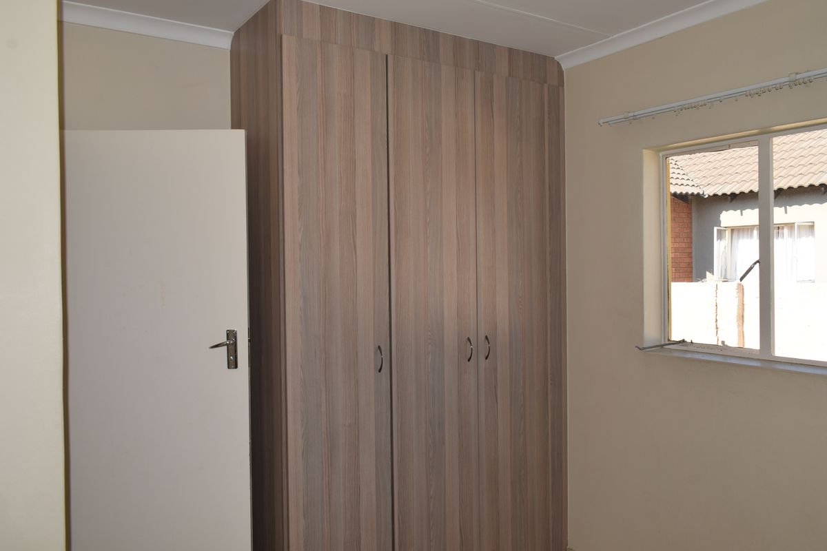 A clean, empty bedroom featuring modern wood-finish built-in cupboards and a window with a curtain rail.