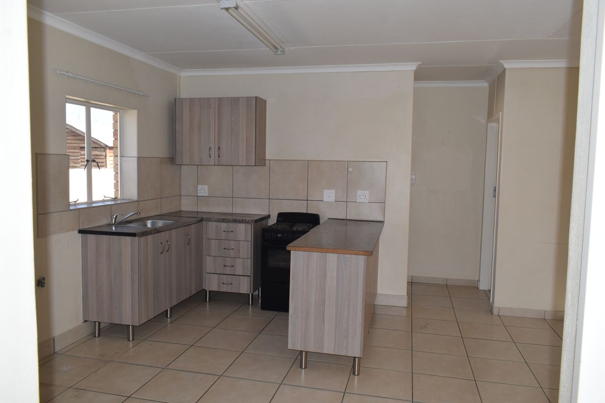 A functional kitchen featuring laminate cabinetry, tiled splashbacks, ceramic floor tiles, and a freestanding stove in an open-plan layout.