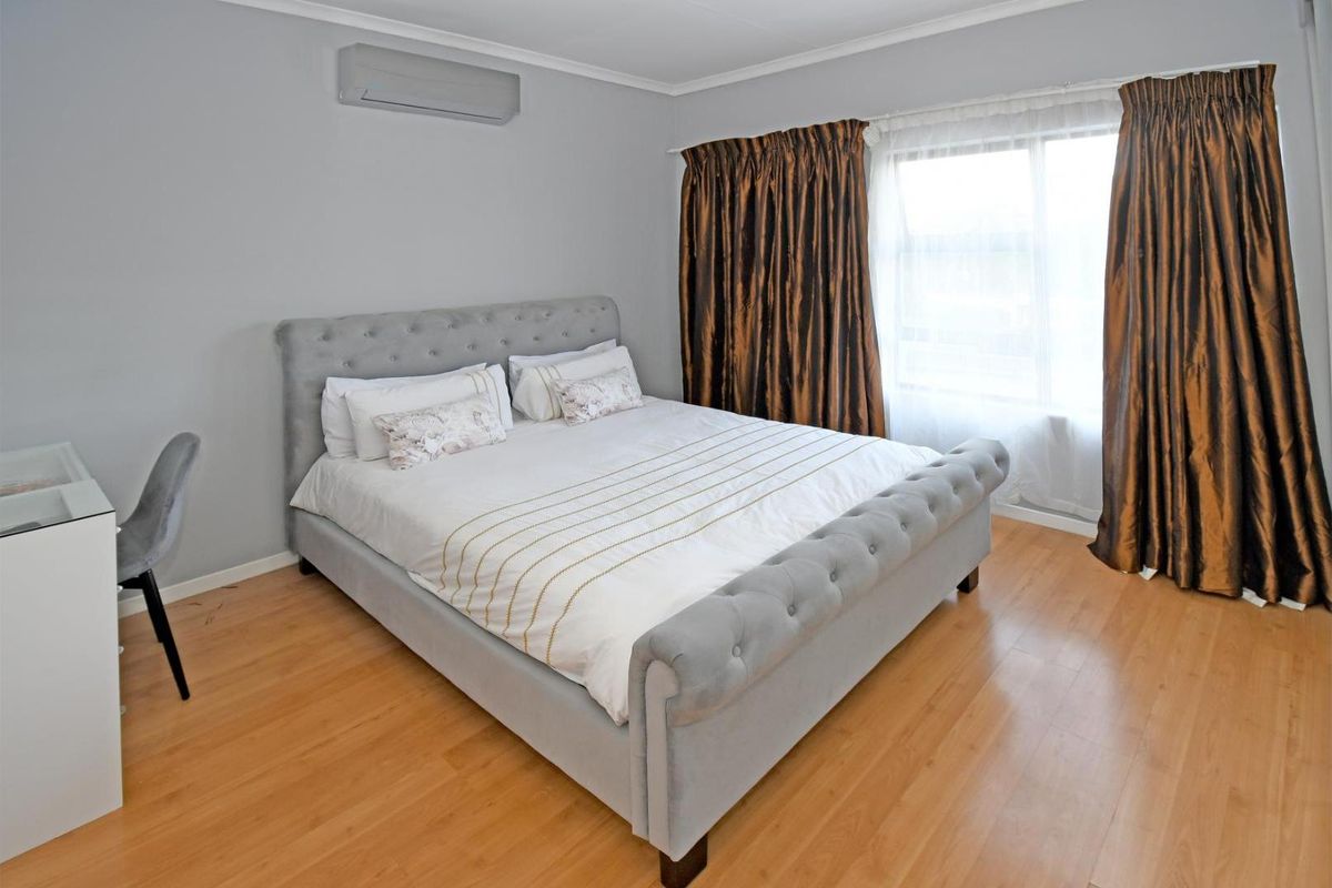 A well-maintained bedroom featuring light wood-look flooring, neutral wall finishes, and a wall-mounted air conditioning unit.