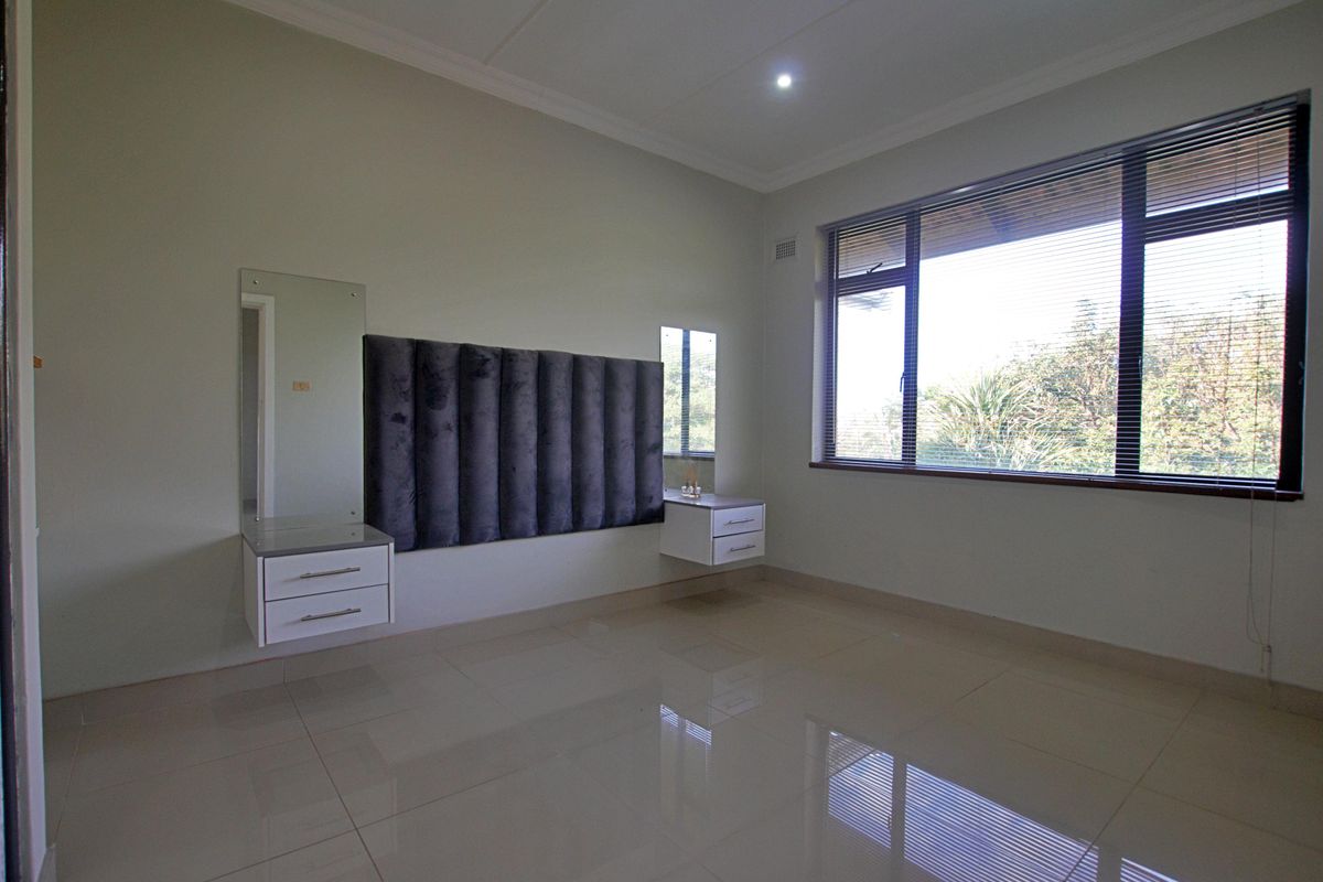 A spacious, well-lit bedroom featuring neutral tiled floors, built-in floating bedside cabinetry, and a modern upholstered headboard panel.