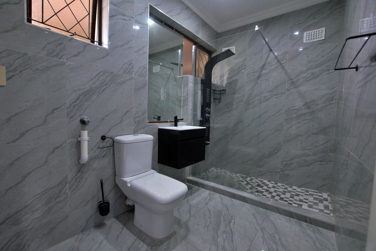 Modern bathroom featuring grey marble-look tiling, a wall-mounted vanity, and a spacious walk-in shower with a glass screen.