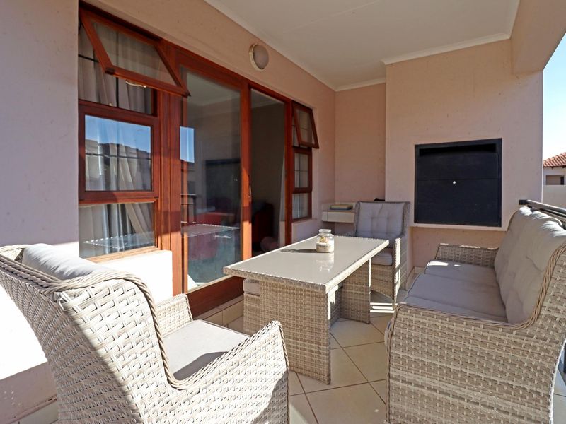 A covered patio area featuring a built-in braai, tiled flooring, and direct access to the interior through wooden-framed glass sliding doors.