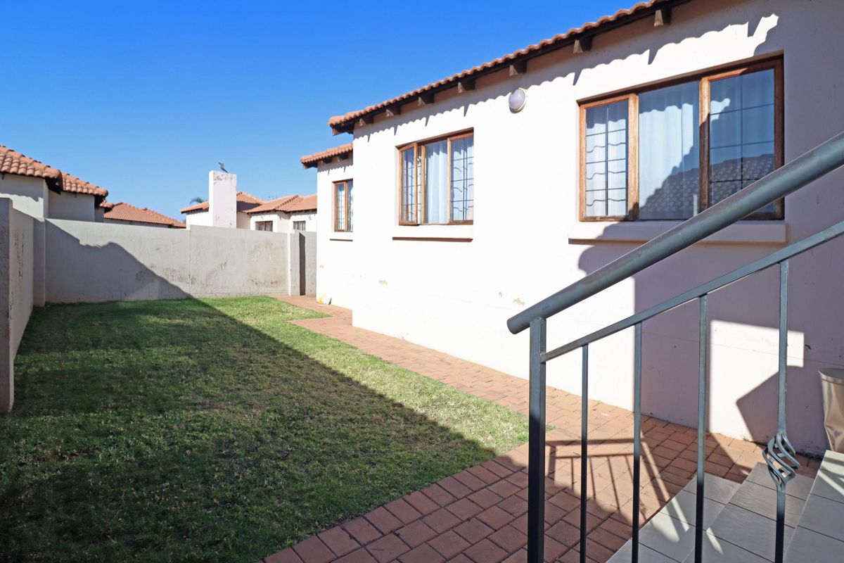 A private rear garden area featuring a paved walkway, lawn, and exterior access to the townhouse with security bars on windows.