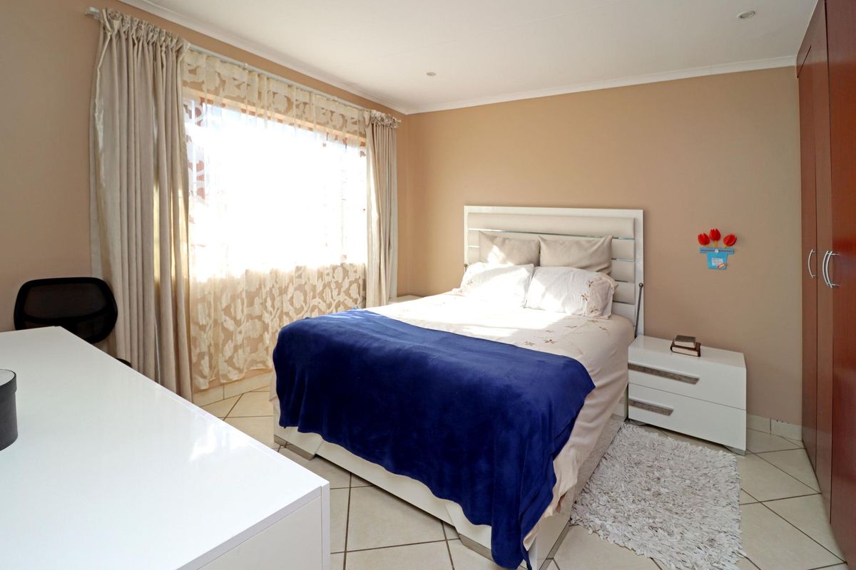 A well-lit bedroom featuring tiled flooring, built-in wooden cupboards, and large windows with curtain tracks.