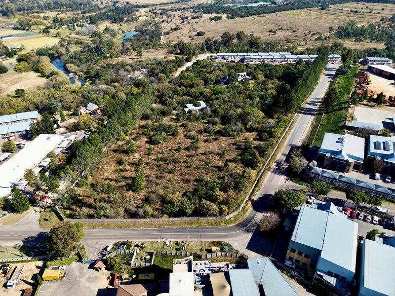 Aerial view of a vacant residential plot featuring established trees and vegetation, situated in a developed area with road access.
