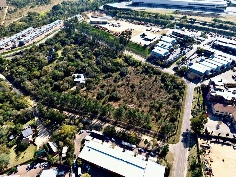 Aerial view of a large, undeveloped residential land parcel surrounded by established trees and adjacent to commercial and industrial infrastructure.
