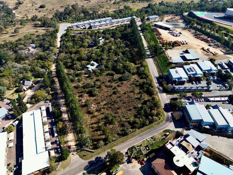 An aerial view of a vacant residential land plot surrounded by established trees and adjacent to existing commercial and residential developments.