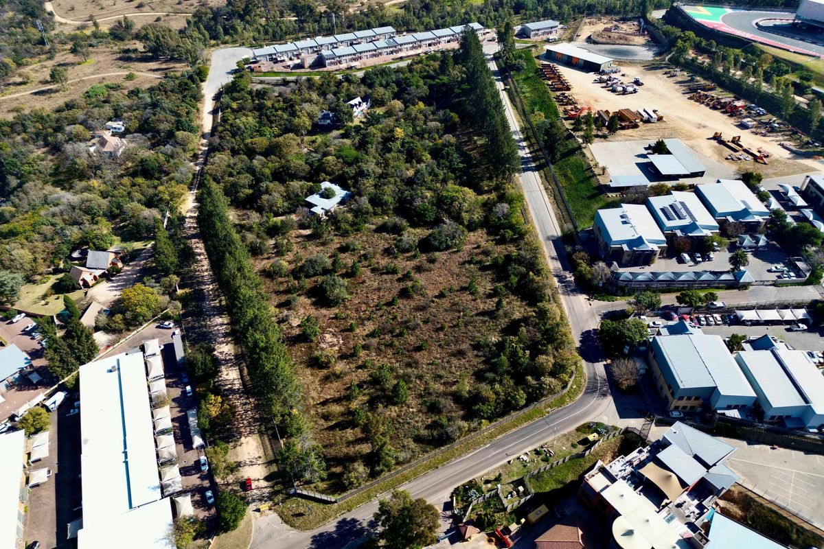 An aerial view of a vacant residential land plot surrounded by established trees and adjacent to existing commercial and residential developments.
