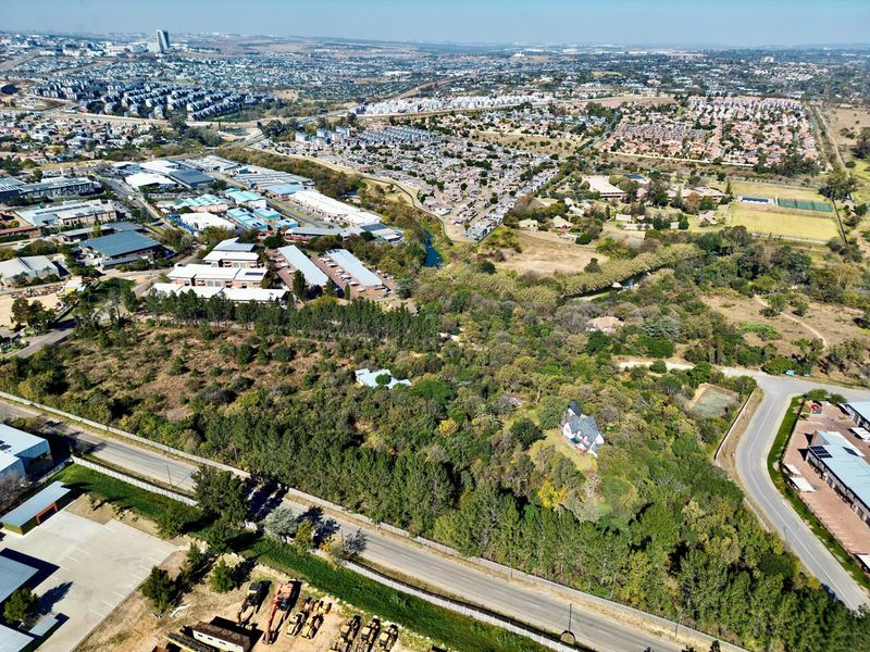 Aerial view of a large, wooded residential land parcel situated in a developed suburban area with surrounding infrastructure and road access.