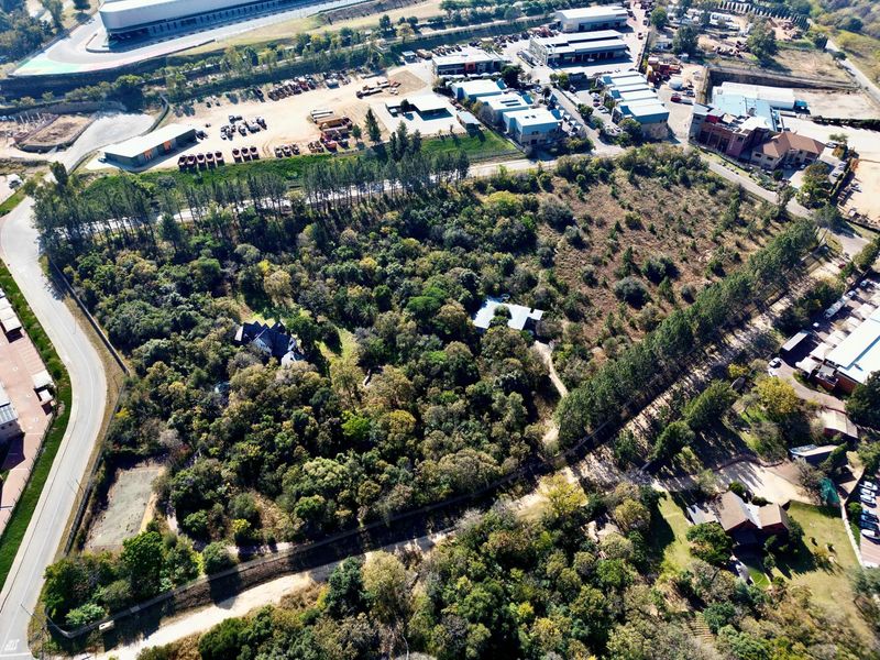 Aerial view of a large, heavily wooded residential plot featuring established trees and existing structures within a suburban landscape.