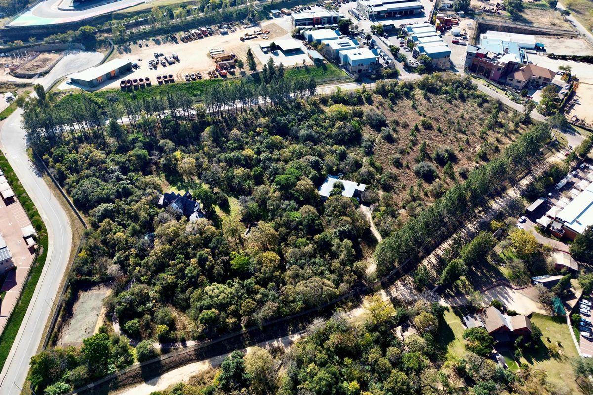 Aerial view of a large, heavily wooded residential plot featuring established trees and existing structures within a suburban landscape.
