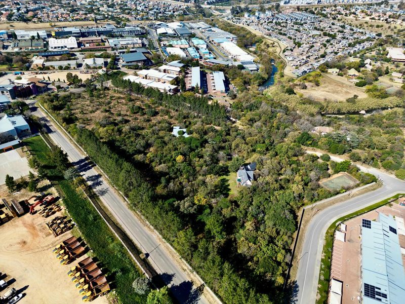 Aerial view of a large, heavily wooded residential land parcel situated near commercial and residential developments.