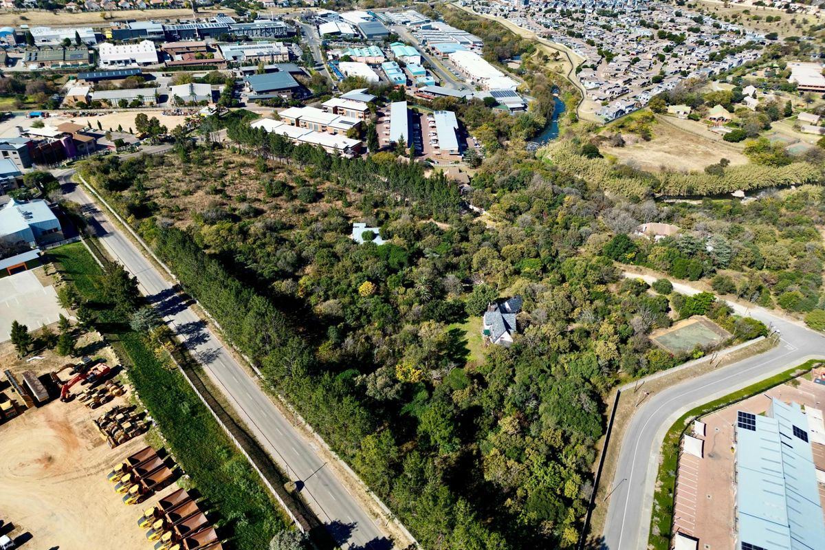 Aerial view of a large, heavily wooded residential land parcel situated near commercial and residential developments.