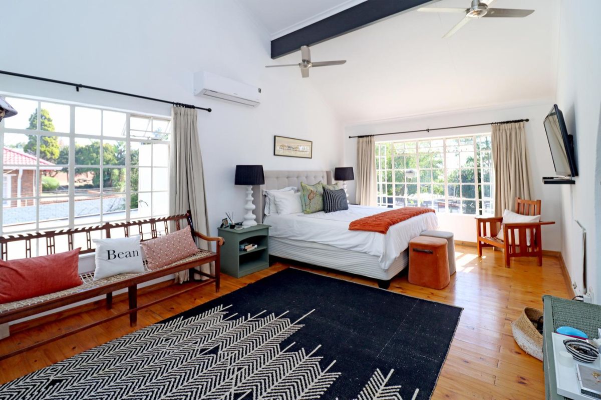 Spacious bedroom featuring vaulted ceilings, exposed beams, polished wooden flooring, and large windows providing ample natural light.