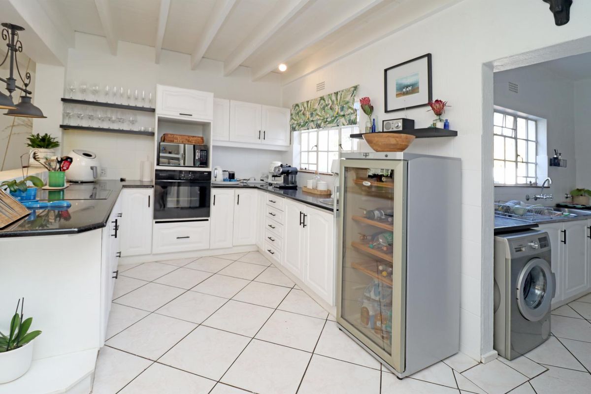 A bright, well-maintained kitchen featuring white cabinetry, dark countertops, tiled flooring, and exposed ceiling beams, with an adjacent laundry area visible.