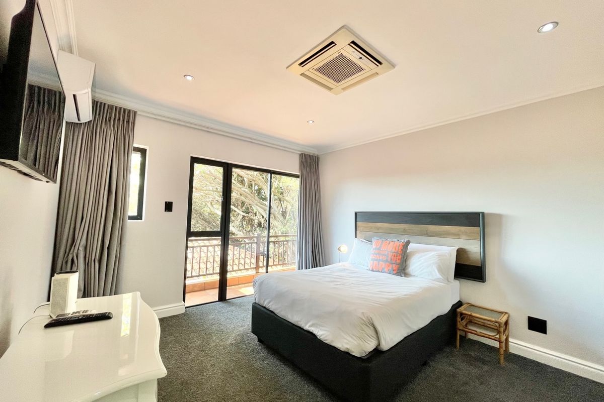 A well-maintained bedroom featuring a ceiling-mounted air conditioning unit, carpeted flooring, and sliding glass doors leading to a private balcony.