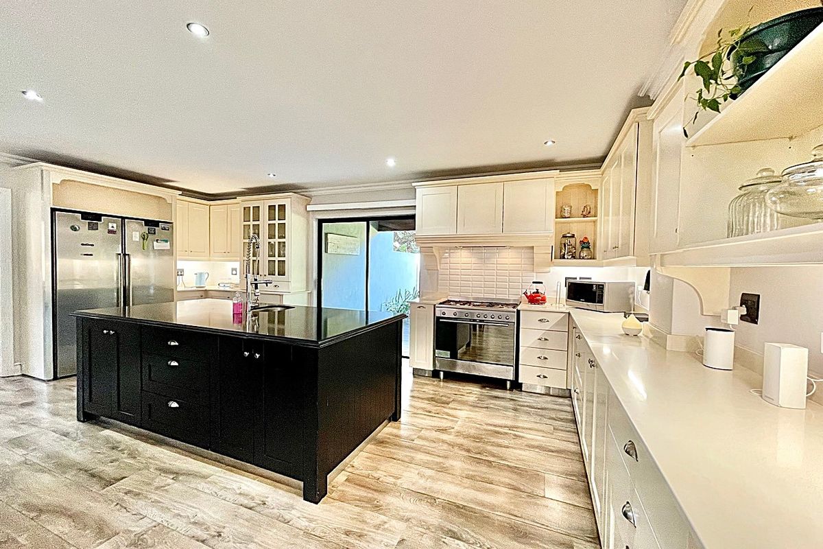 Spacious kitchen featuring a large central island with a dark finish, light-colored cabinetry, stone countertops, and integrated stainless steel appliances.