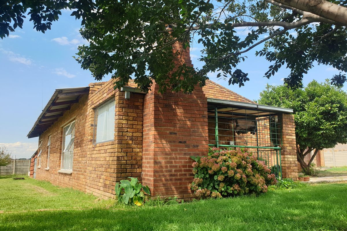 A view of the rear exterior of a face brick house featuring a brick chimney and a covered patio area set within a garden.