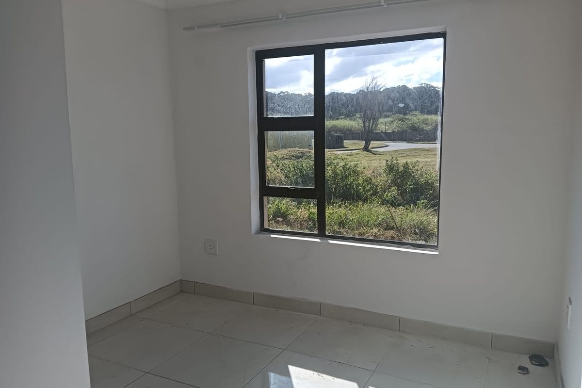 A bright, empty bedroom featuring neutral tiled flooring and a large aluminium-framed window with views of the surrounding landscape.