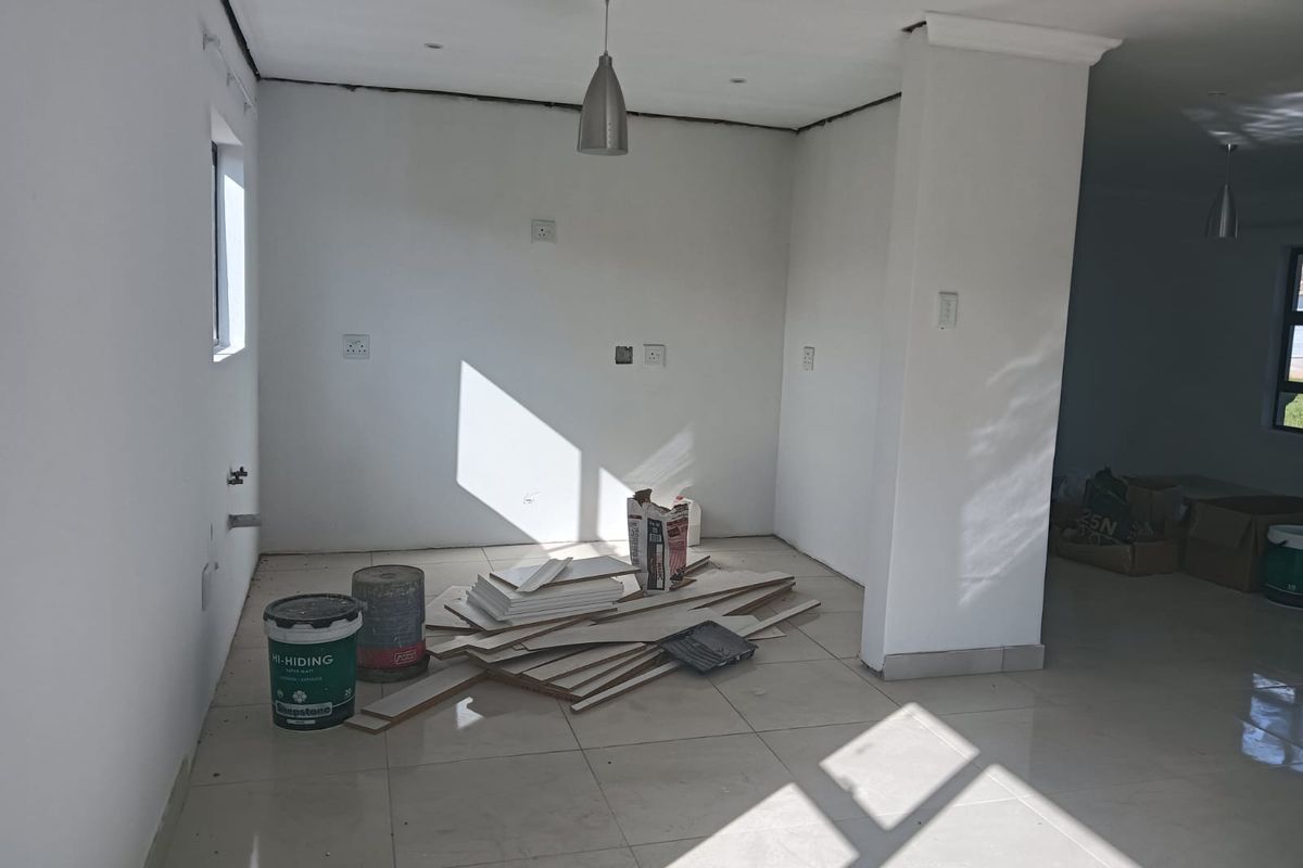 An unfinished kitchen area featuring tiled flooring, pendant lighting, and plumbing points, currently undergoing renovation with exposed wall edges and wiring.