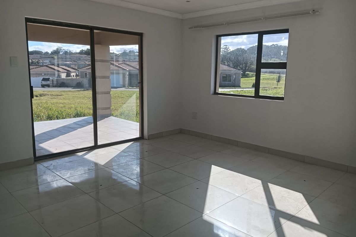 A bright, empty living area featuring large tiled floors, aluminium window frames, and a sliding glass door leading to an outdoor patio.