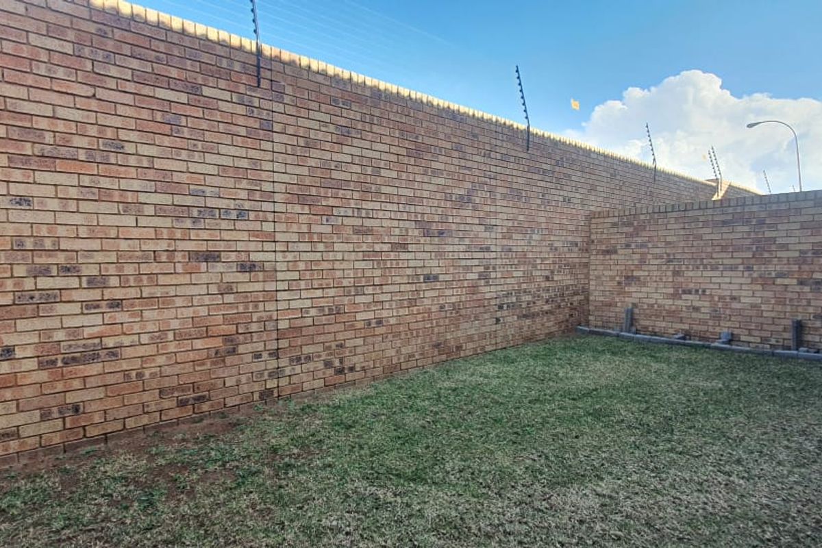 A private rear garden area featuring a high brick boundary wall with integrated electric fencing and a small lawn.