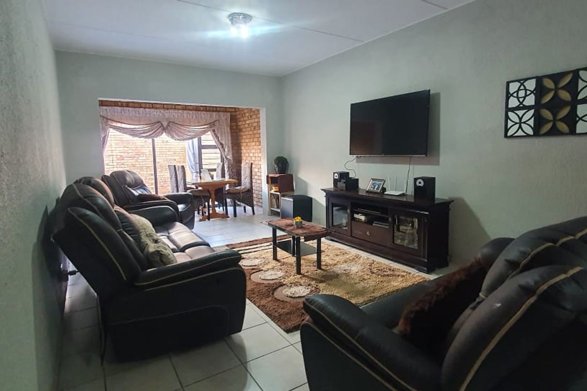 A comfortable living room featuring tiled flooring and an exposed brick accent wall leading to an adjacent dining area.
