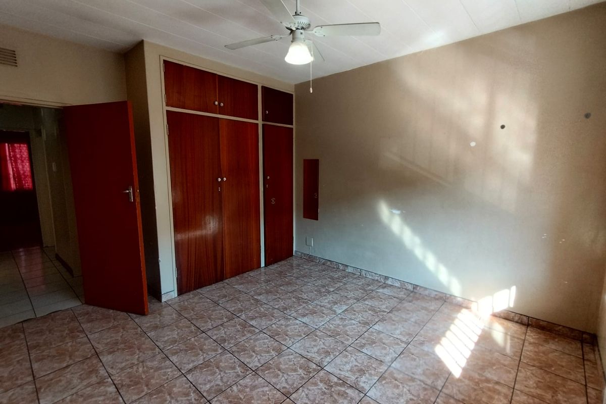 A bedroom featuring built-in wooden cupboards, tiled flooring, and a ceiling fan, offering a functional and neutral living space.