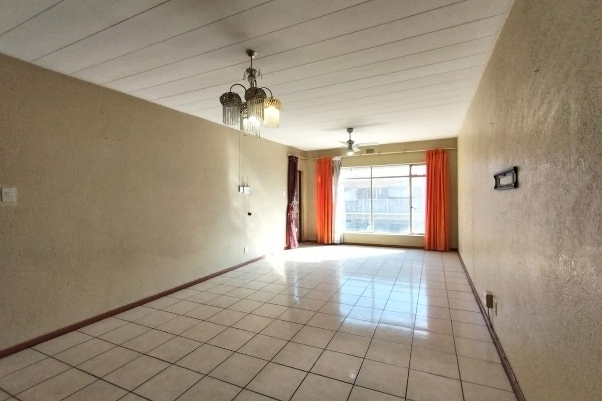 A spacious, empty living area featuring tiled flooring, a ceiling fan, and a decorative chandelier, offering a blank canvas for potential renovation.