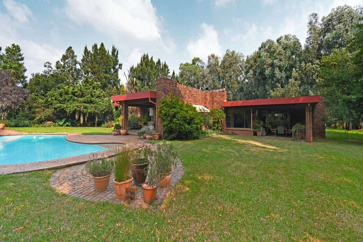 Rear view of the property featuring a swimming pool, brick facade, and a covered patio area set within a spacious landscaped garden.