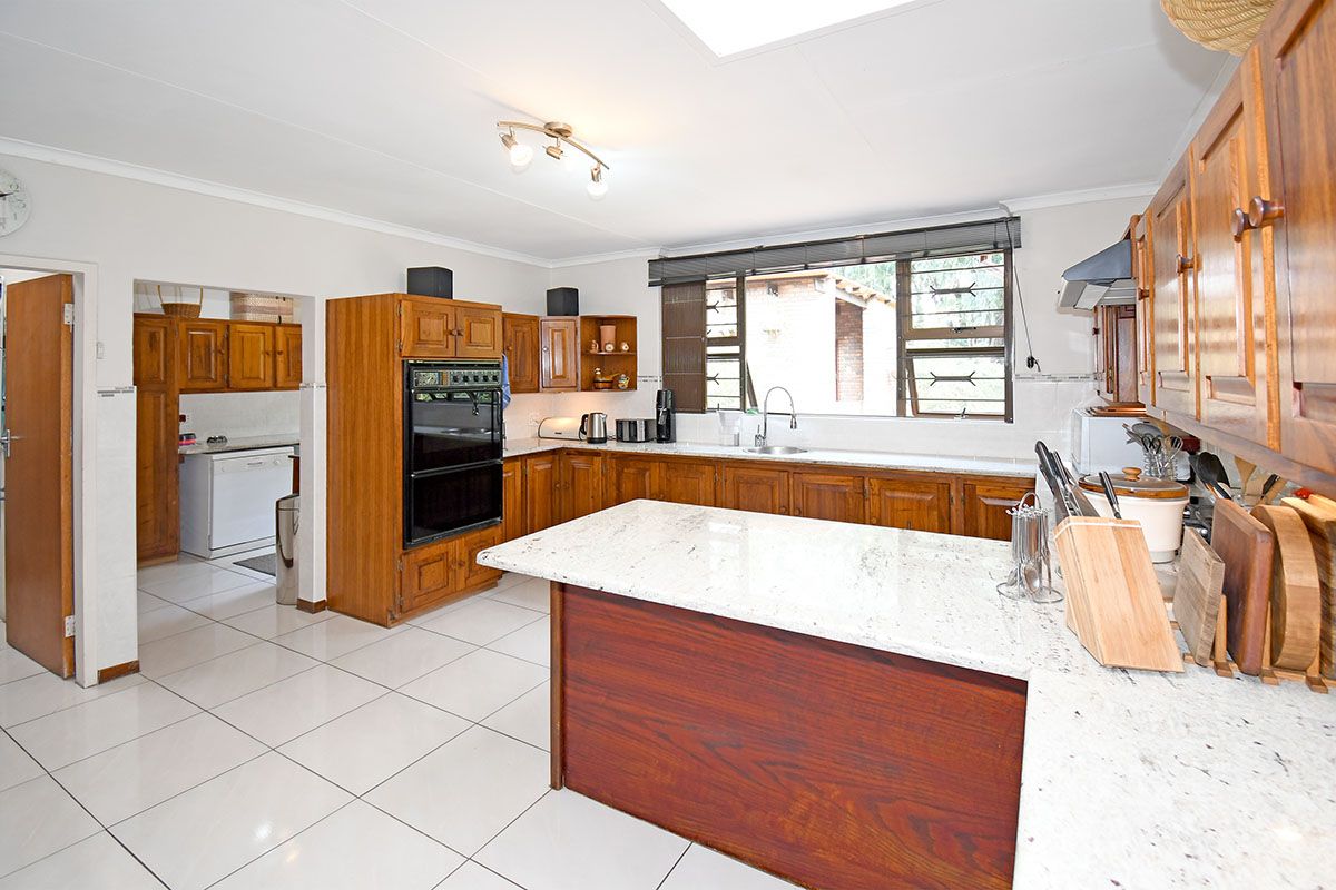 Spacious kitchen featuring traditional wooden cabinetry, granite countertops, a double wall oven, and a convenient adjoining scullery area with tiled flooring.