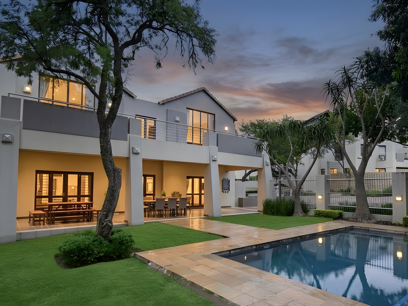 Rear view of a modern two-story apartment building featuring a covered patio, upper balcony, landscaped garden, and a private swimming pool.