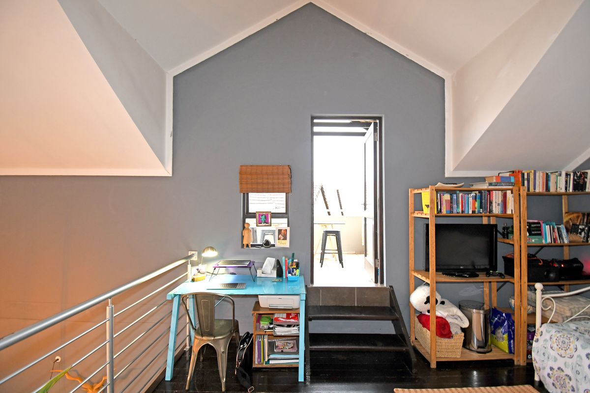 A loft-style bedroom featuring vaulted ceilings, dark timber flooring, a metal balustrade, and direct access to an outdoor balcony area.