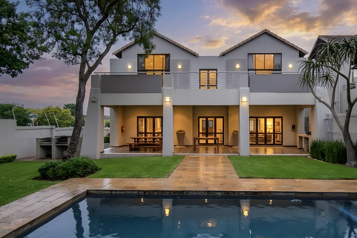 Rear view of a modern double-story apartment featuring a swimming pool, paved patio, balcony, and landscaped garden area.