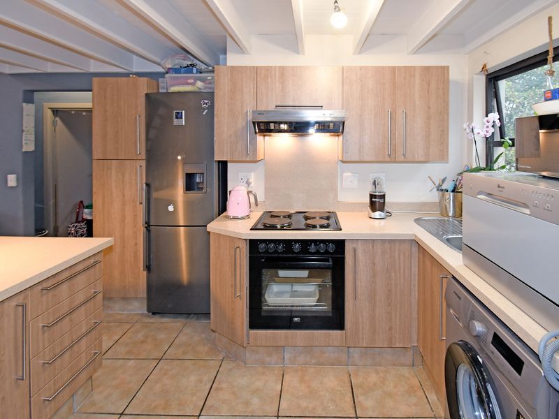 Functional kitchen featuring light wood-finish cabinetry, laminate countertops, built-in oven and hob, tiled flooring, and exposed ceiling beams.