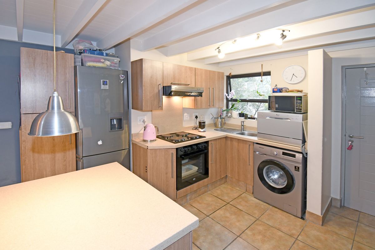 A functional kitchen featuring wood-look cabinetry, tiled flooring, exposed ceiling beams, and integrated appliances including an oven, hob, and extractor fan.