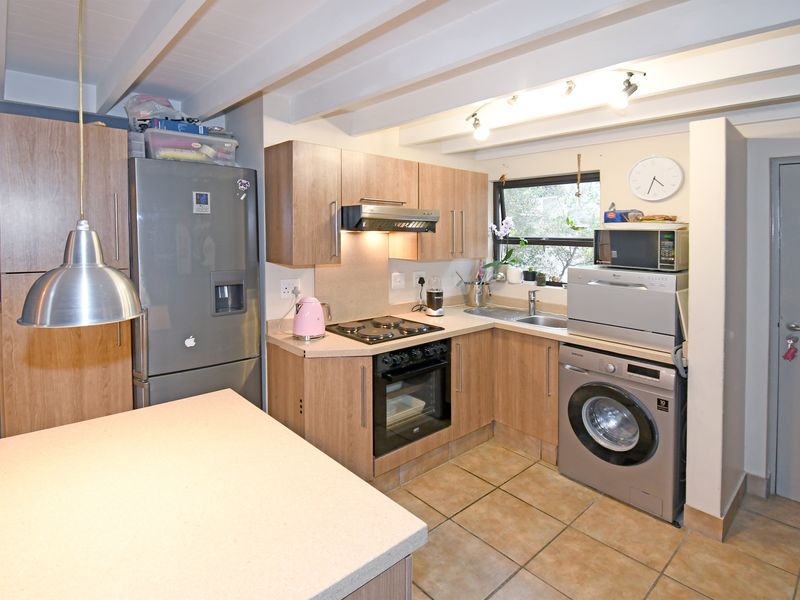 A functional kitchen featuring wood-look cabinetry, tiled flooring, exposed ceiling beams, and integrated appliances including an oven, hob, and extractor fan.