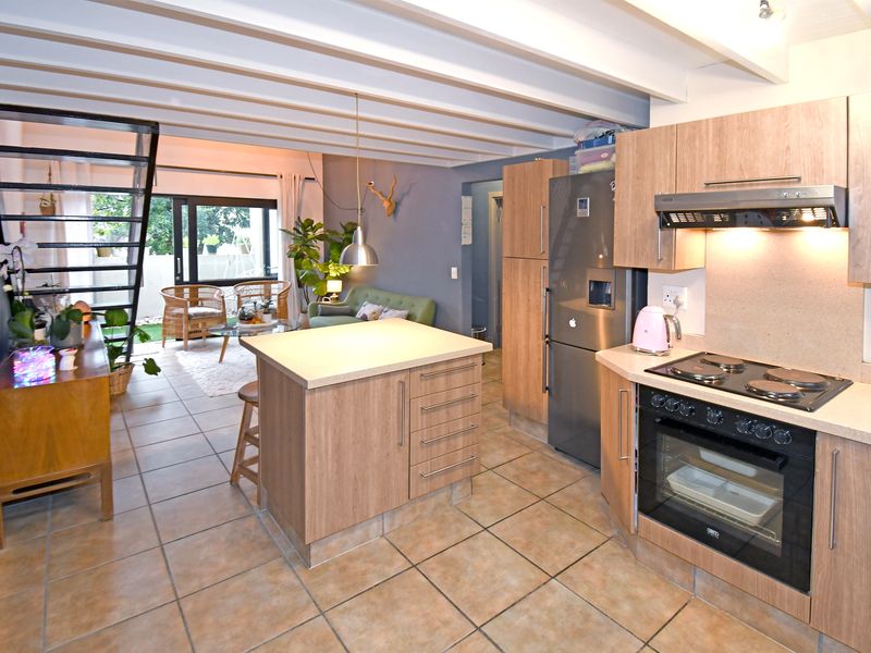Open-plan living area featuring a modern kitchen with a central island, built-in appliances, tiled flooring, and exposed ceiling beams leading to a lounge space.