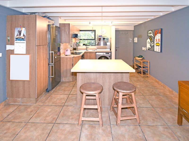 A functional kitchen featuring a central island, wood-finish cabinetry, tiled flooring, and exposed ceiling beams, providing a practical layout for cooking and dining.