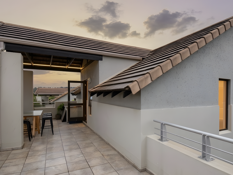 A modern, covered balcony featuring tiled flooring, a metal balustrade, and a pitched roof, offering a clean and well-maintained outdoor living space.