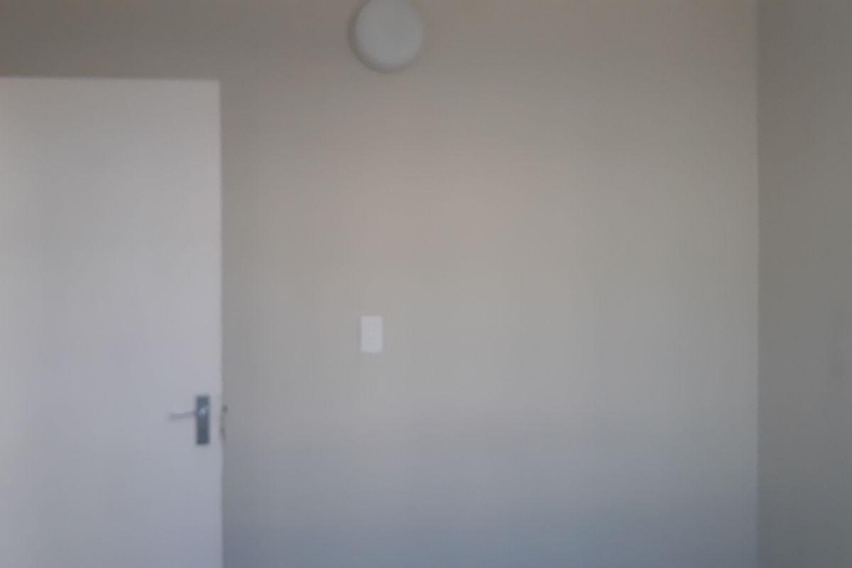A simple, empty bedroom interior featuring neutral walls, a standard door, and a ceiling light fixture.
