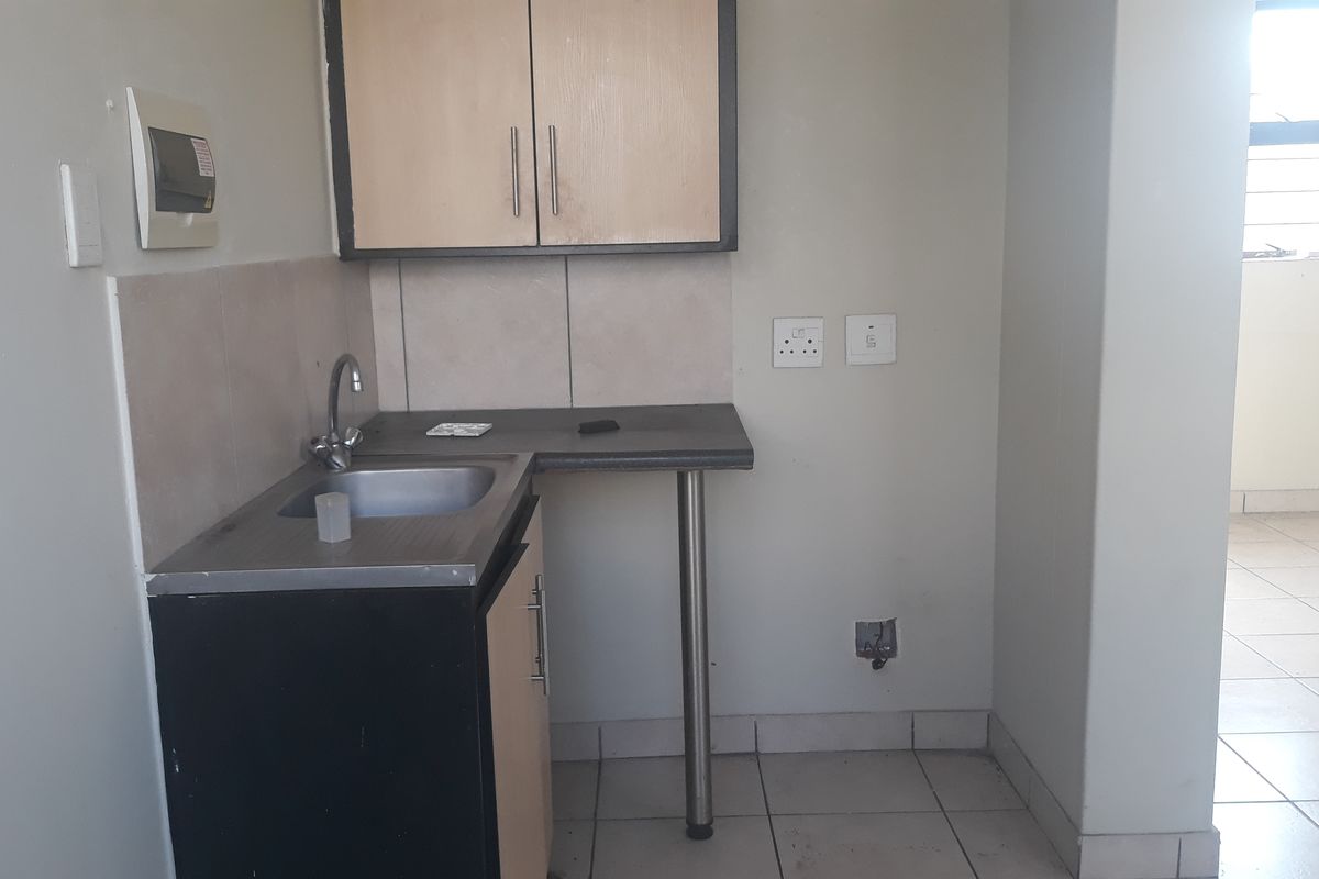 A compact kitchen area featuring basic cabinetry, a stainless steel sink, tiled splashback, and tiled flooring, currently in need of cosmetic updates.