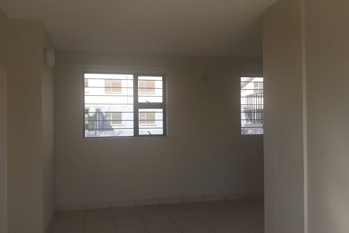 An empty, neutral-toned living area featuring tiled flooring and windows fitted with security bars, offering a blank canvas for interior design.