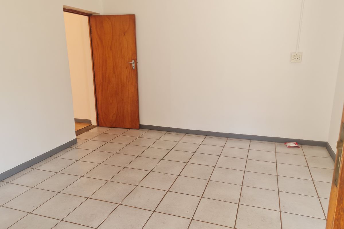 A vacant bedroom featuring neutral tiled flooring, white walls, and a wooden door, providing a clean and versatile space ready for personalization.