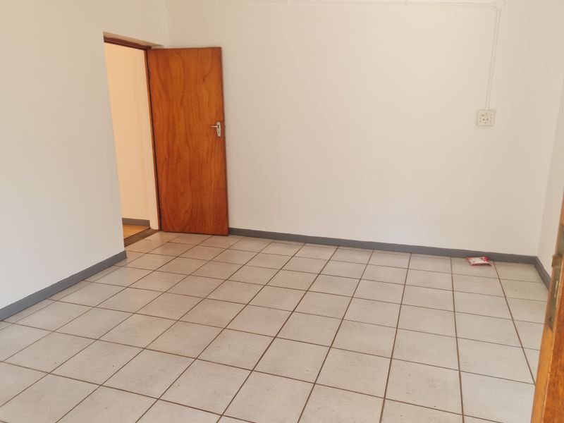 A vacant bedroom featuring neutral tiled flooring, white walls, and a wooden door, providing a clean and versatile space ready for personalization.