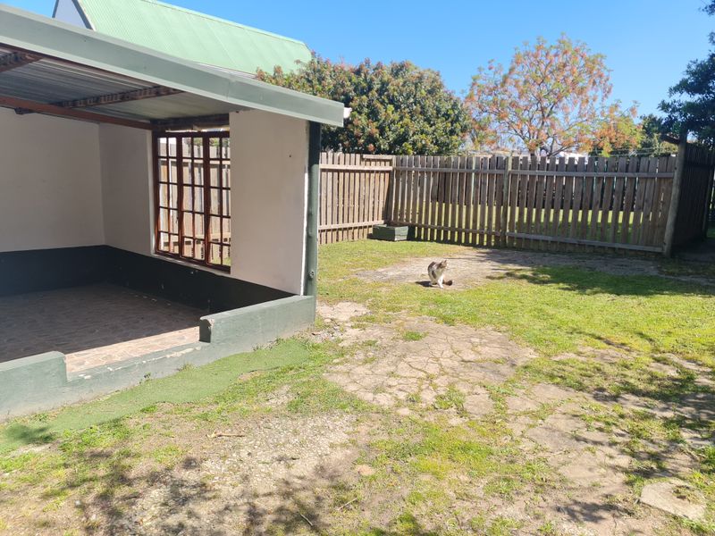 A covered outdoor patio area featuring tiled flooring, adjacent to a private garden with timber fencing and worn lawn space.