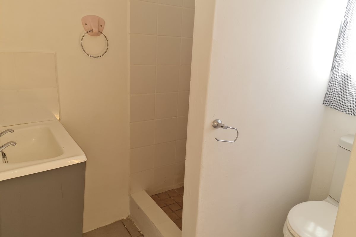 A functional bathroom featuring a vanity basin, a tiled shower cubicle, and a toilet, presenting a dated aesthetic ready for modernization.