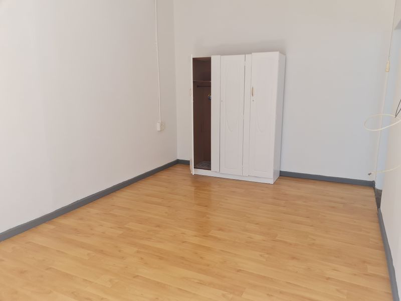 A bright, empty bedroom featuring light wood-look laminate flooring and neutral white walls, providing a clean and versatile space ready for personalization.