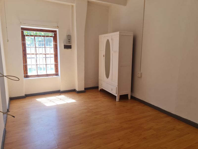 A bedroom featuring laminate flooring, a timber-framed window with security bars, and an electrical distribution board.