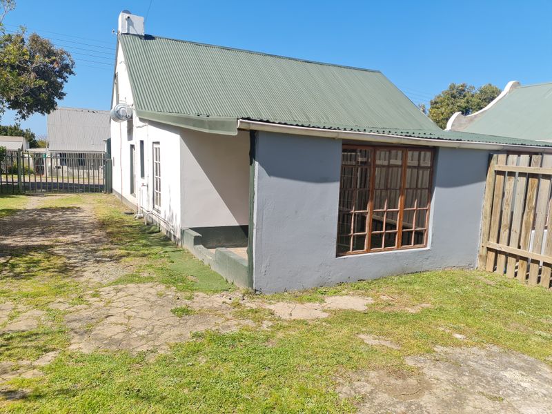 Rear view of the property featuring a corrugated metal roof, timber-framed windows, and a private garden area with a timber fence.